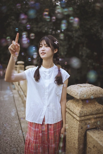 一个小女孩站在喷泉前 她的手指着天空 空中吹着肥皂泡。