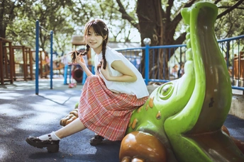 一个小女孩坐在公园里的滑梯上 用一个小孩的相机给另一个小孩拍照。