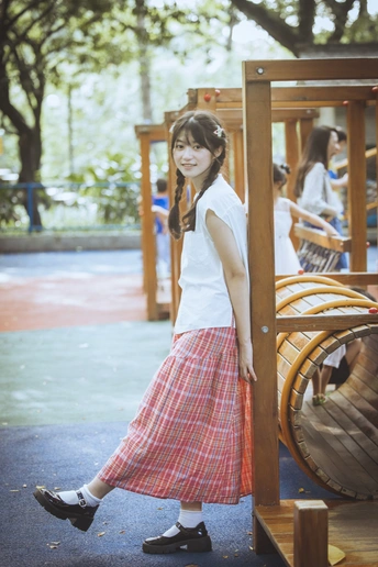 一个小女孩穿着裙子站在公园的游乐场上