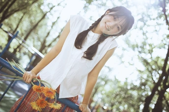 一位穿着白色连衣裙的年轻女子站在公园里 手里拿着一把伞 旁边停着一辆自行车。