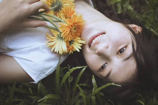 一位年轻女子躺在草地上 手里拿着一朵黄色花