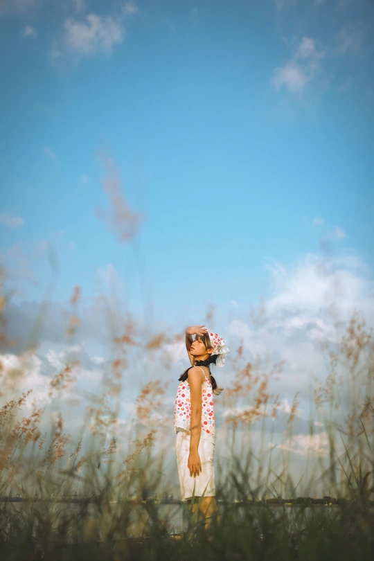 一个小女孩穿着裙子站在一片高草地的蓝天下