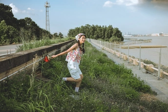 一位年轻女子沿着河岸边行走 河岸上长满了青草和植物。