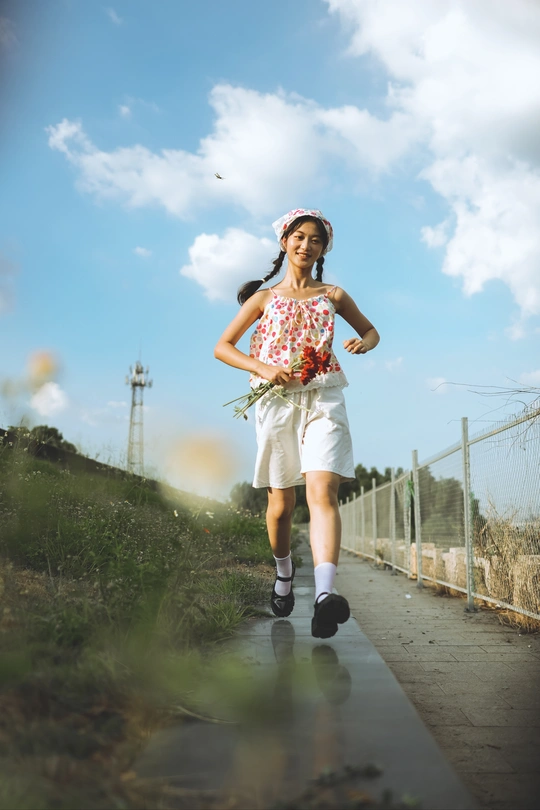 一位年轻女子手拿花和伞 沿着有水坑的道路走下小径。