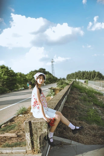 一个穿着连衣裙的年轻女子坐在公路路边的长椅上