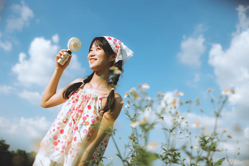 一位穿着白色连衣裙的年轻女子 手持一朵白色花 背景是蓝天下的田野。