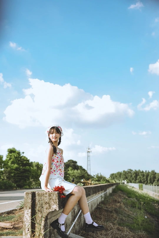 一个小女孩穿着花裙子坐在桥上的墙上