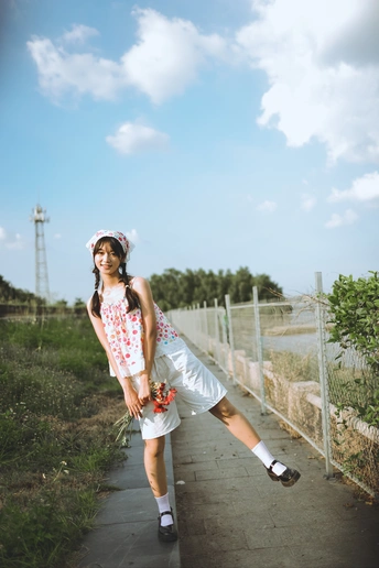 一个穿着裙子的年轻女孩站在人行道上 旁边有一道围墙 她正踩着滑板。