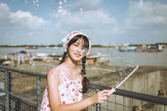 一位年轻女子拿着一个吹泡机在河边吹泡泡。