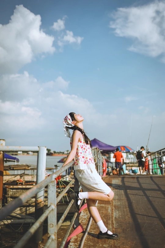 一位穿着连衣裙的年轻女子站在码头上 俯视着水面 一个小女孩儿正在栏杆上探头。