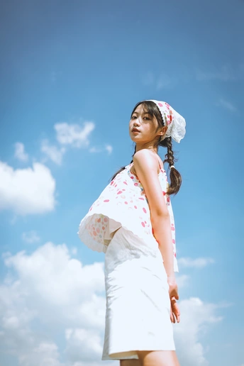 一个穿着白色连衣裙的年轻女子站在多云的蓝色天空中