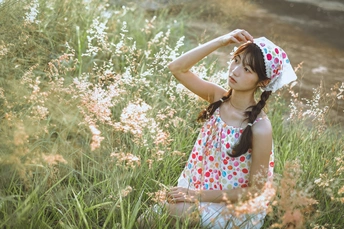 一个小女孩穿着裙子坐在一片高草花丛中 头上有花。