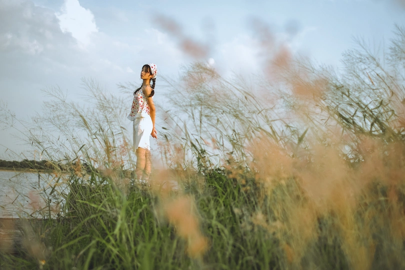 一位穿着白色连衣裙的年轻女子站在一片高草地上 凝视着天空。