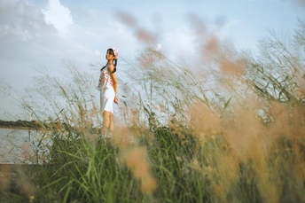 一位穿着白色连衣裙的年轻女子站在一片高草地上 凝视着天空。