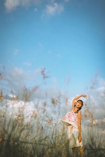 一个穿着连衣裙的年轻女子站在一片高草地上 她的双臂伸向天空。