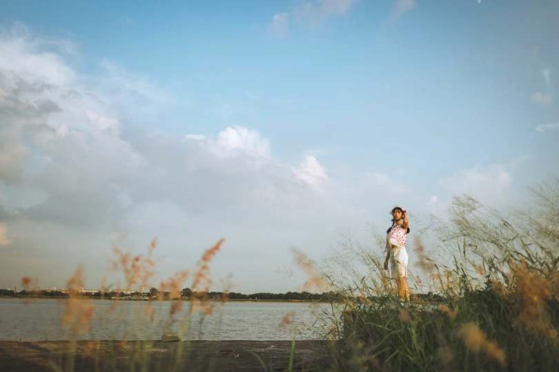 一位穿着婚纱的年轻女子在水边的田野中亲吻她的丈夫