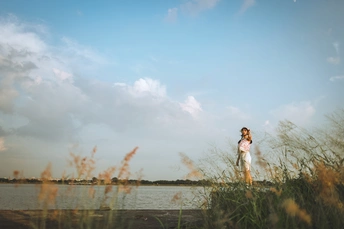 一位穿着婚纱的年轻女子在水边的田野中亲吻她的丈夫