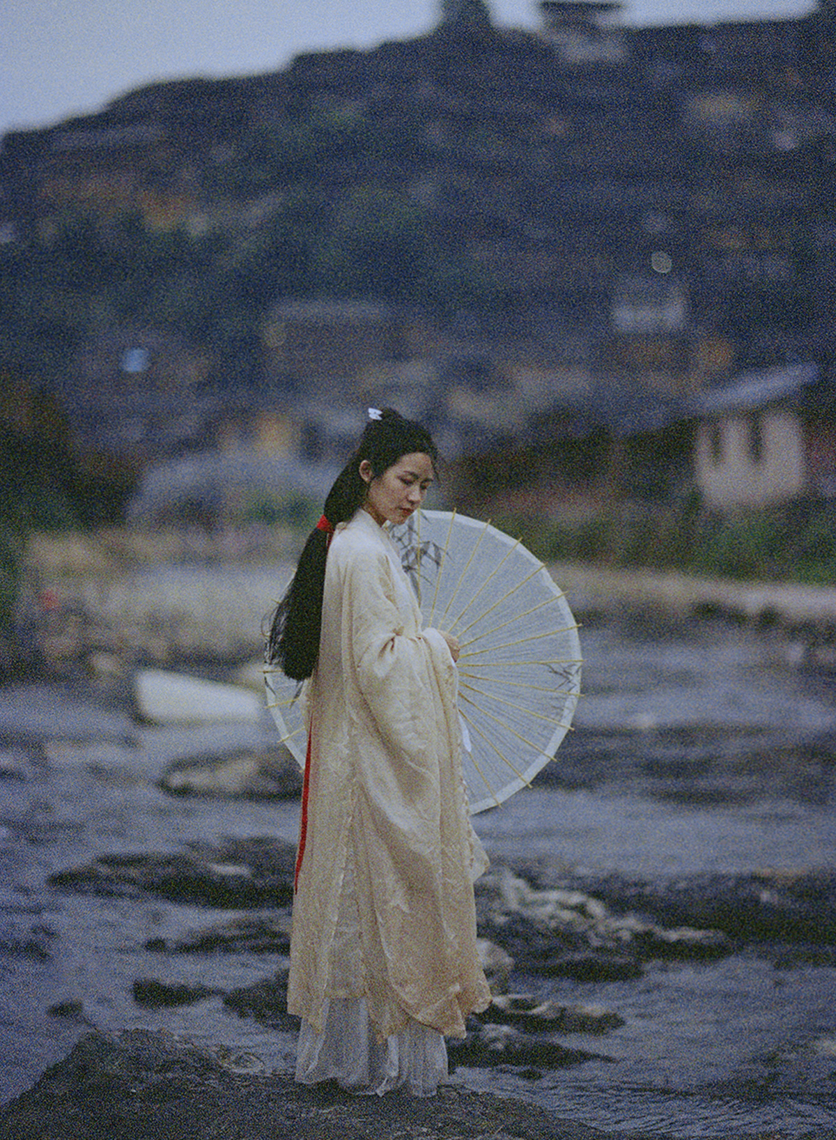 一位穿着白色连衣裙 手持雨伞沿着河流岸边行走的女人