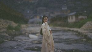 一位穿着白色连衣裙的年轻女子站在一条河流的水中