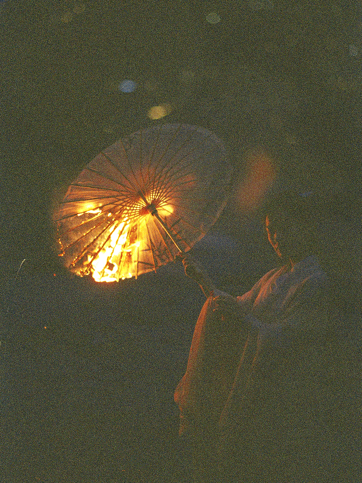 一个在黑暗夜晚坐在火旁边 手持打开的雨伞的女人