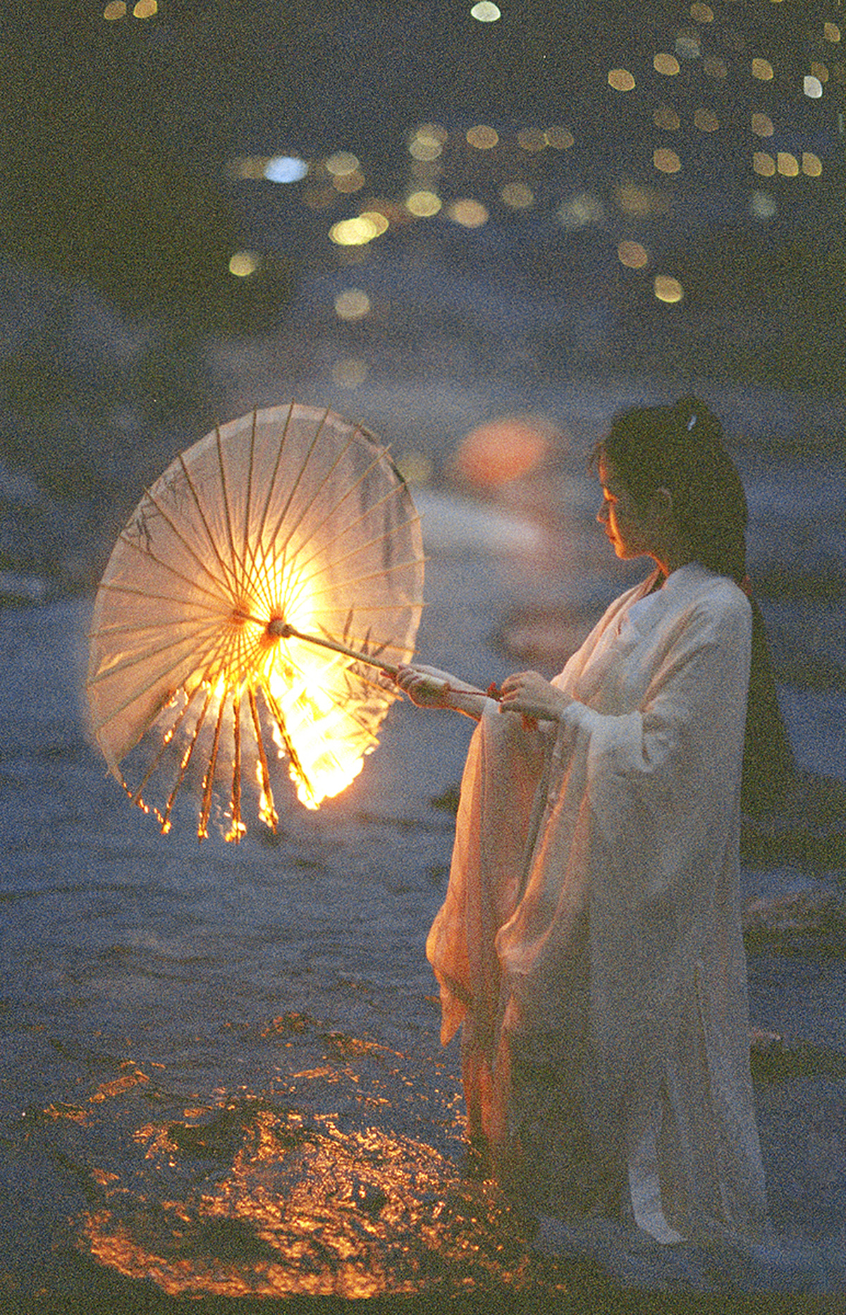 一个穿着白色连衣裙的年轻女子手持一盏灯的雨伞站在夜晚的水中