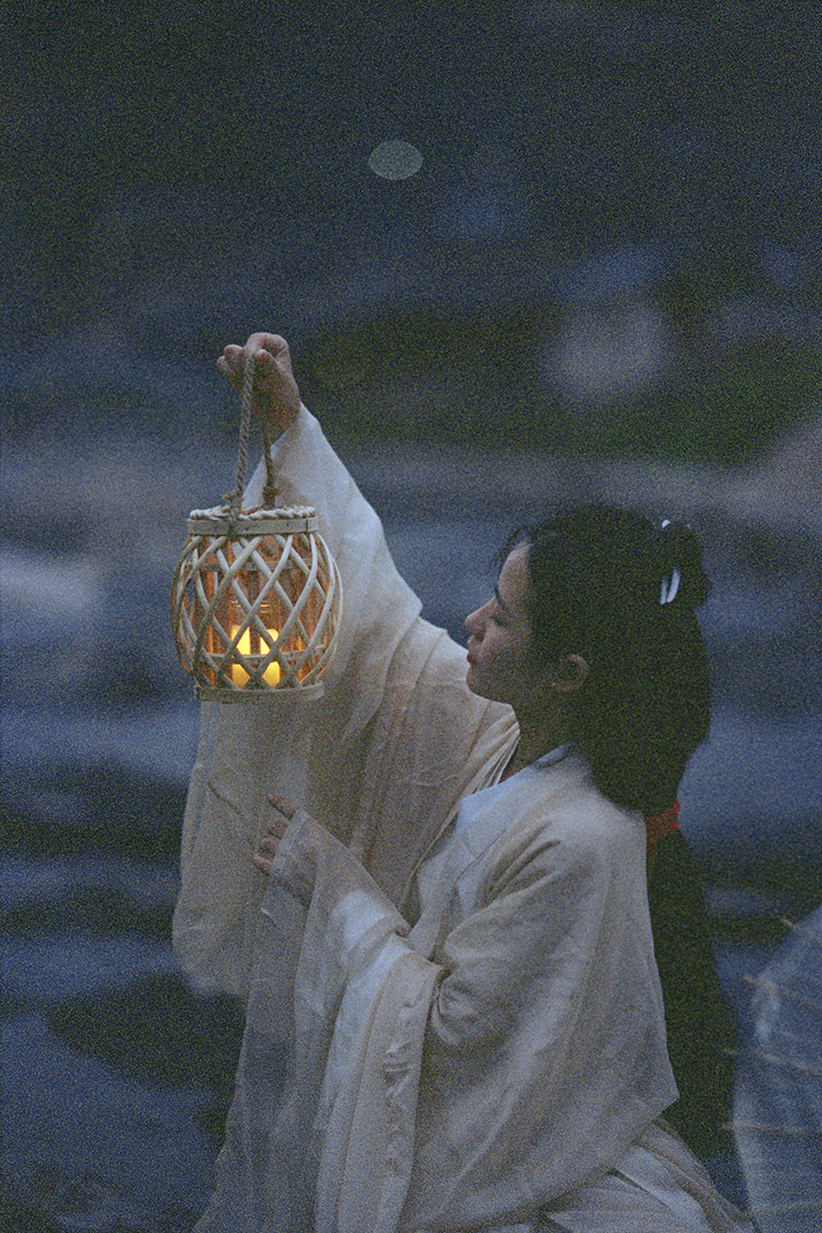 一位身着白色长袍的女子手持点燃的蜡烛坐在雕像旁边