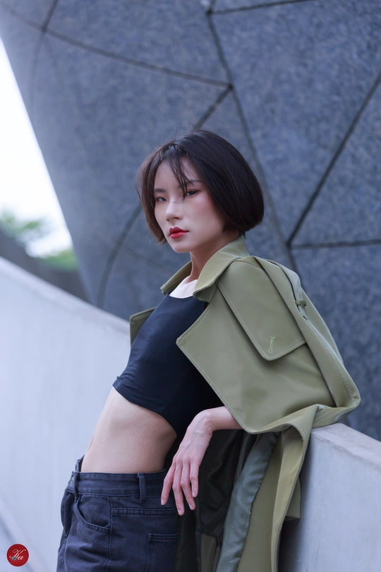 一个穿着黑色上衣和绿色外套的女人站在街上的墙上