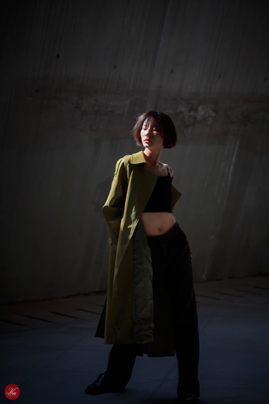 一个穿着绿色外套的孕妇站在一个后面有水泥墙的黑暗房间里