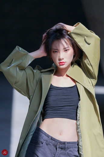 一位身穿绿色外套的年轻女子在黑色背景前摆姿势