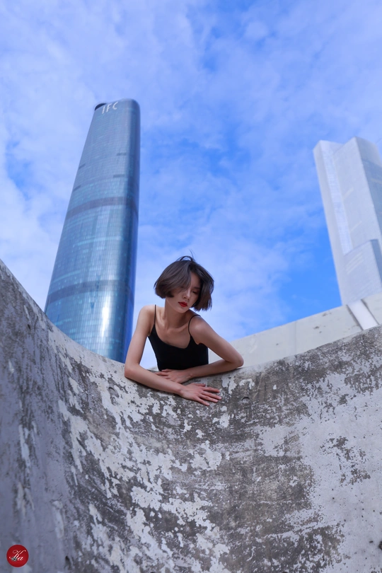 在一座背景是摩天大楼的城市里 一名年轻女子靠在墙上