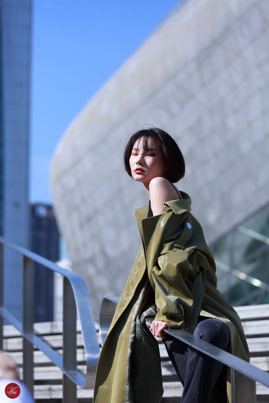 一位身穿绿色风衣的女士在一栋大楼前摆姿势