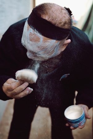 一个老人脸上涂着粉末 手里拿着一杯东西。