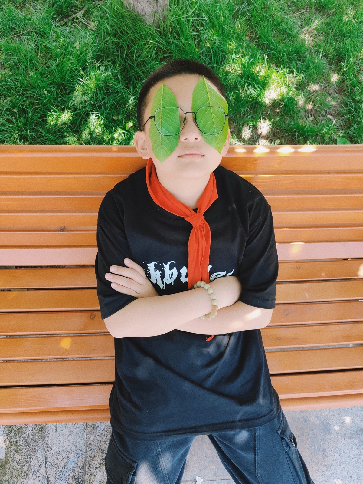 一个年轻的男孩坐在公园长椅上 脸上有一片叶子 双手交叉遮住脸。
