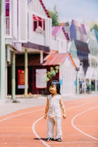 一个小女孩在街边走 背景是房子。