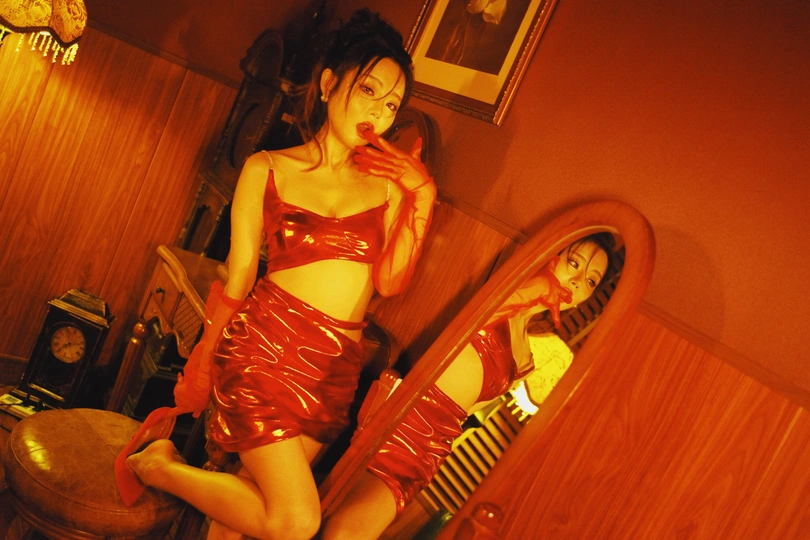 一位穿着红裙子的年轻女子站在一个凳子上 前面有一面镜子。