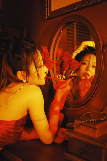 一位穿着红裙子的年轻女子手里拿着花 正看着镜子里的自己的倒影。