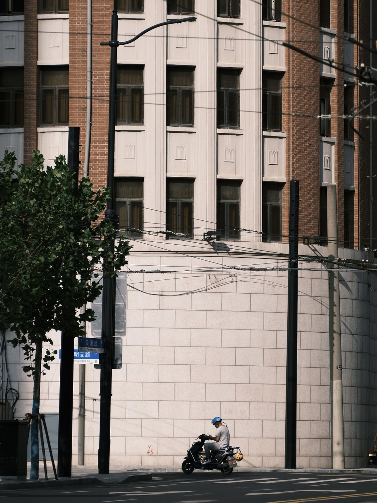 一名男子骑着摩托车在一栋高楼旁的街道上行驶