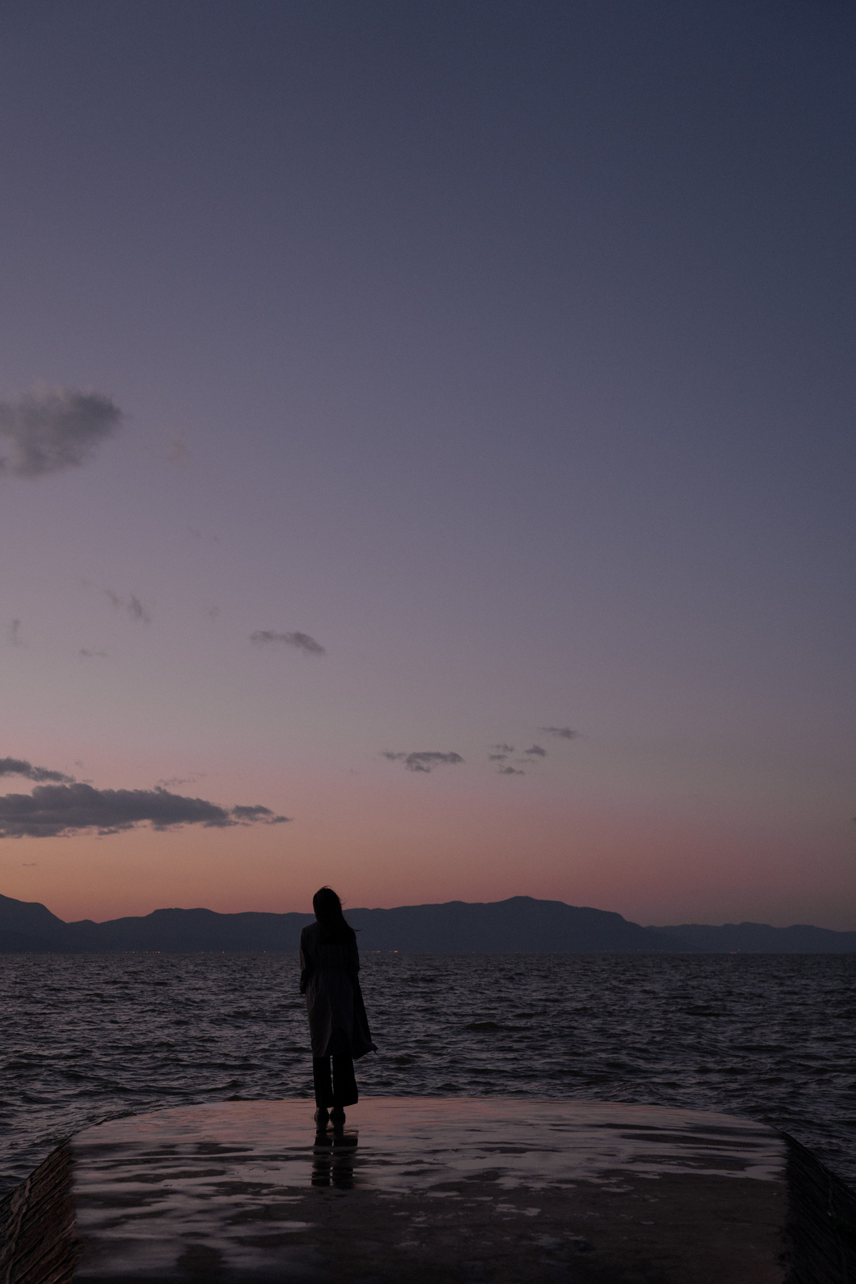 黄昏时分 一位妇女站在码头上眺望大海 落日余晖笼罩着一片水域