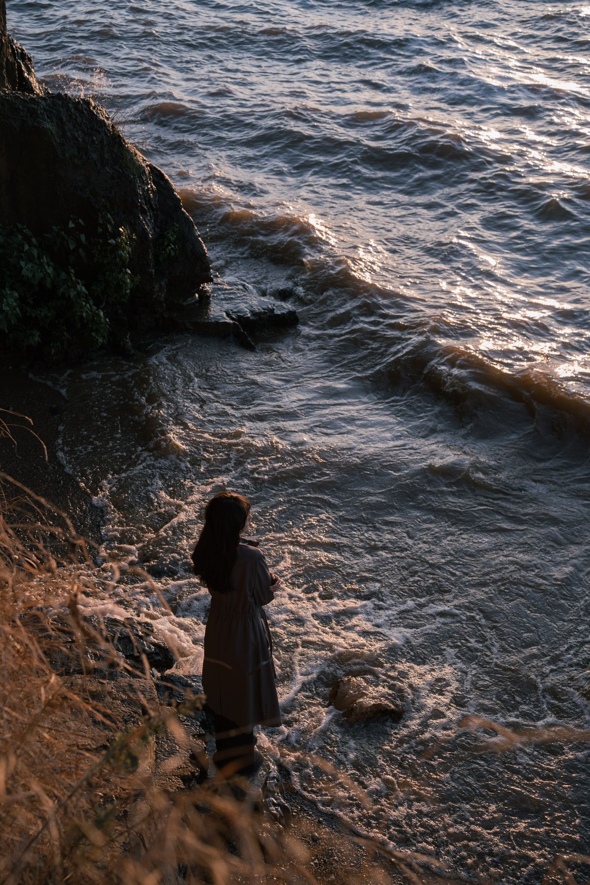 日落时 一个小女孩坐在海边 而一个年轻人站在岩石上眺望大海