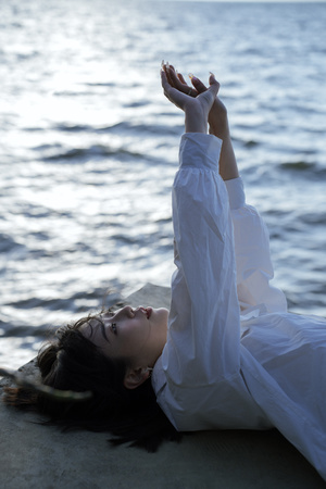 一位身穿白色连衣裙的年轻女子躺在海滩上 双手漂浮在水面前