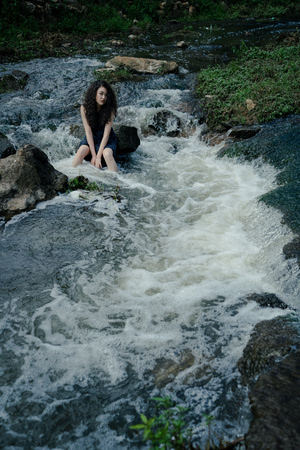 一位年轻女子坐在溪流中的岩石上
