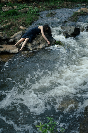 一个年轻男孩躺在一条溪流中的岩石上
