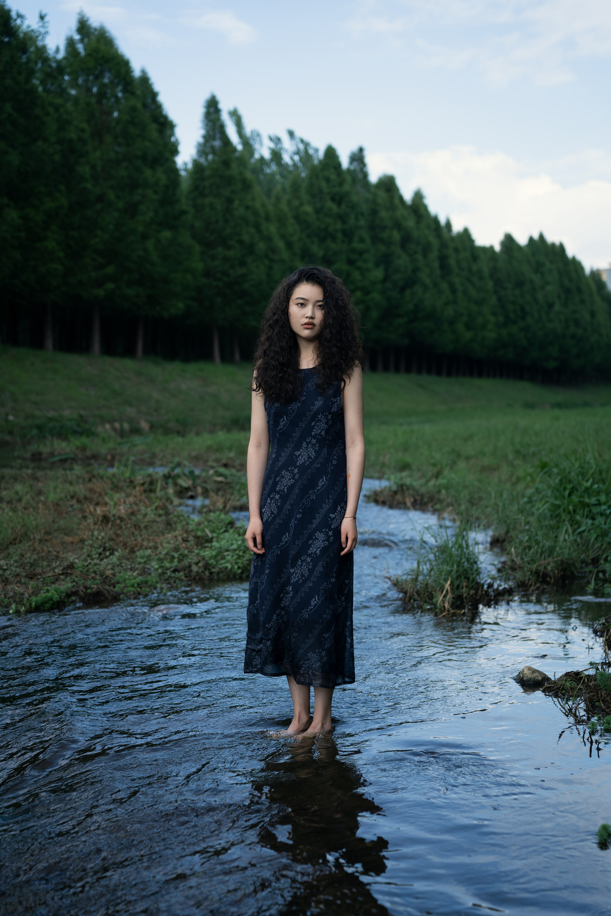 一位穿着连衣裙的年轻女子站在一股水流中 手里拿着一把雨伞 这片田野看起来像一个泥潭。