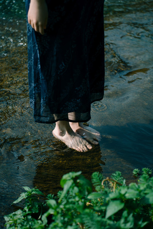 一位穿着连衣裙的女人站在浅水溪流中 双脚浸在水中