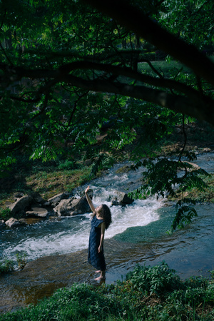 一位穿着连衣裙 带着伞 站在森林或树林中的溪流中的女人