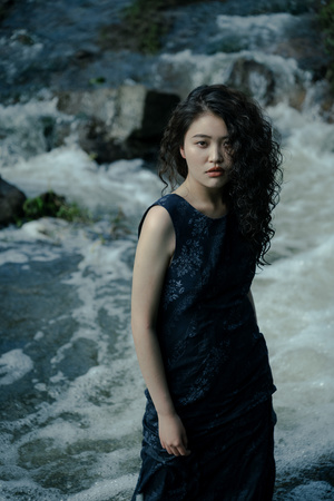 美丽的年轻女子穿着黑色连衣裙在河边或小溪中为肖像摆姿势
