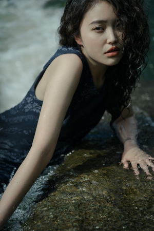 一位湿发年轻女子在河中的一块岩石上为肖像摆姿势