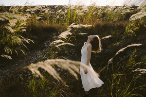 一个穿着白色连衣裙的年轻女子站在一片高草地里