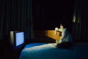 一个年轻男孩或女孩坐在黑暗的房间里 晚上在床上看电视。