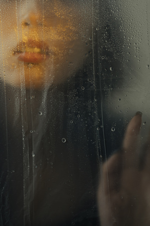 一个人正在窗户边看着雨滴打在玻璃上 一个人拿着伞。